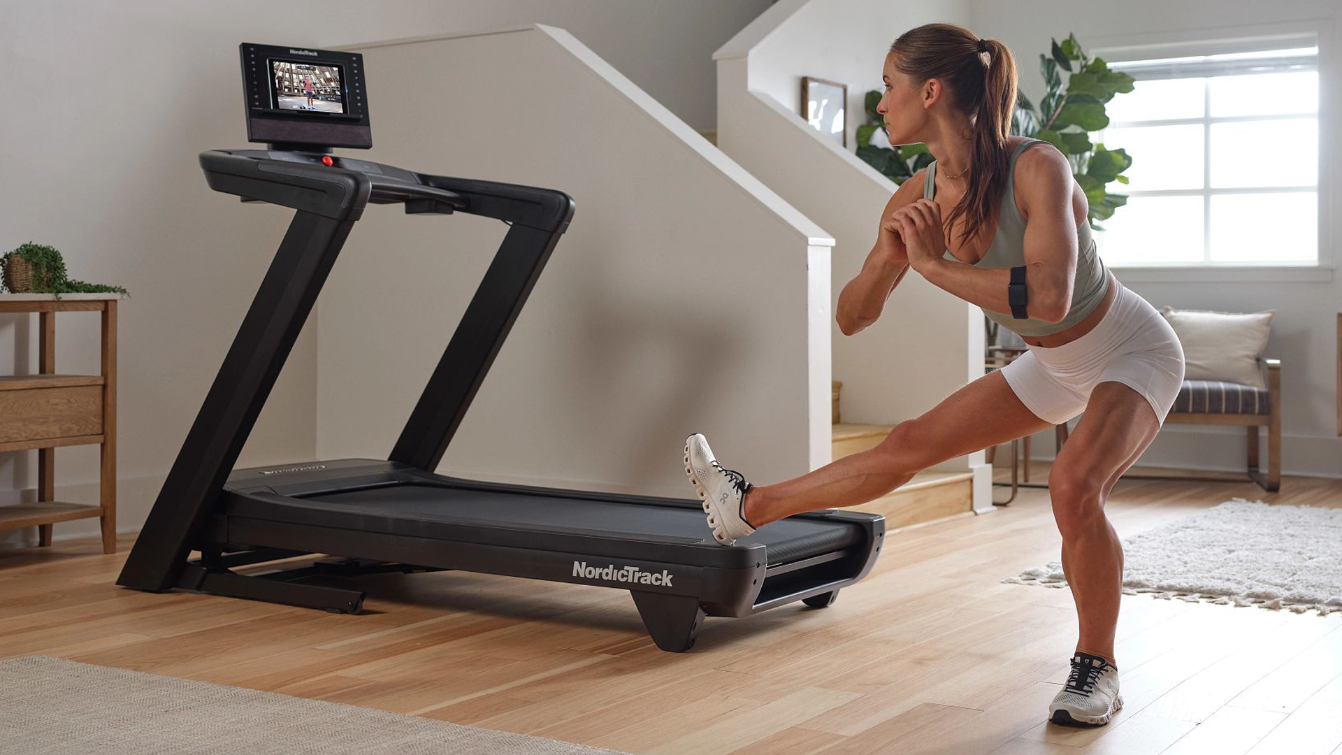 Woman doing one legged pose next to her Commercial LE Treadmill using her device to show iFit content