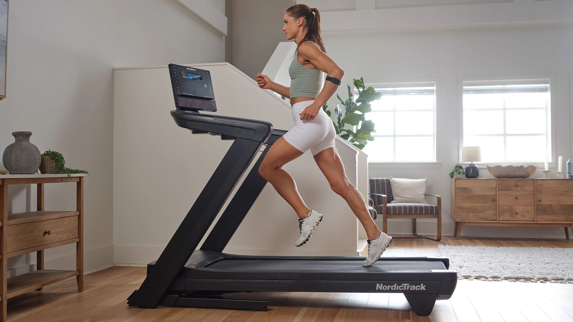Woman running on a NordicTrack Commercial LE Treadmill in a modern living room with a 7-inch LCD display visible