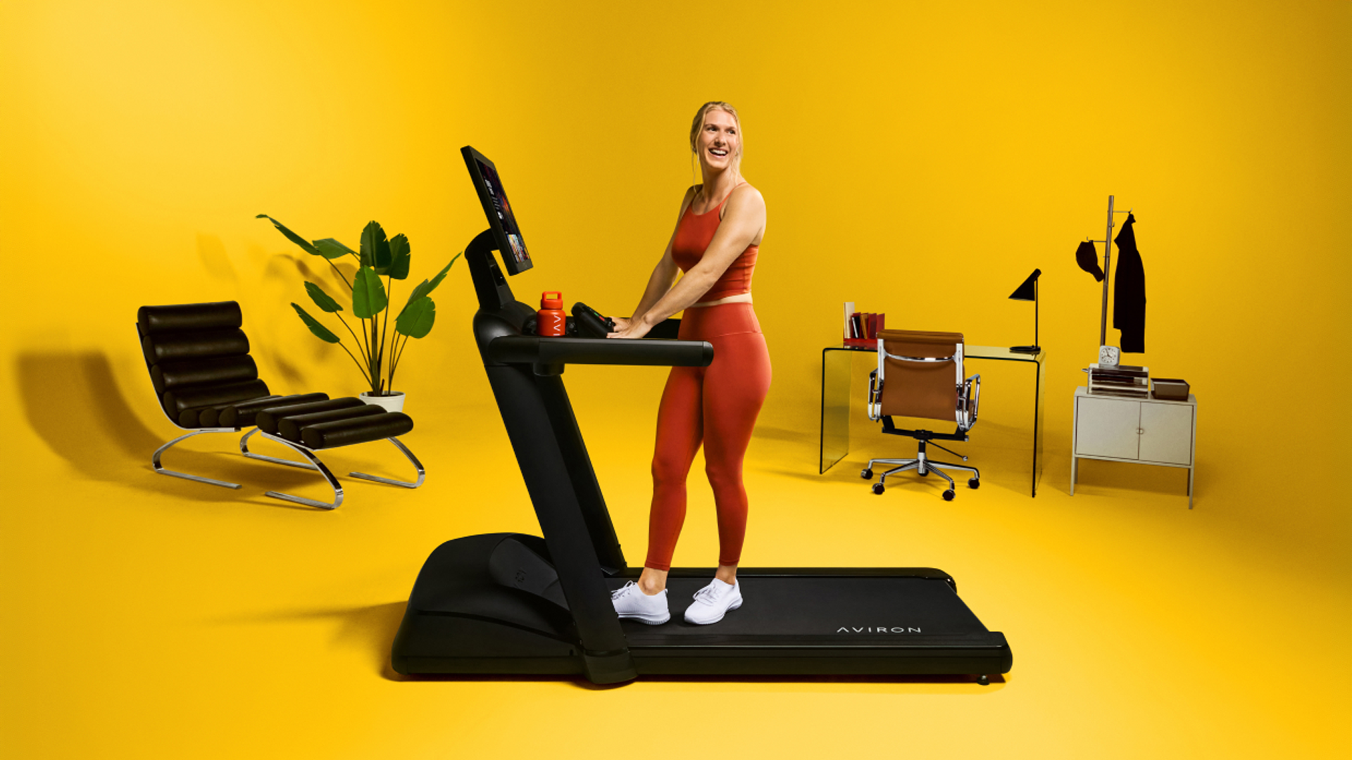 Woman walking on the Aviron Victory Treadmill Plus in bright yellow studio