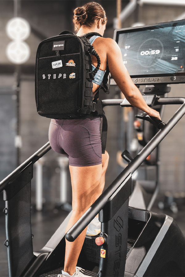 Woman working out on STEPR with her All-In Ruck bag