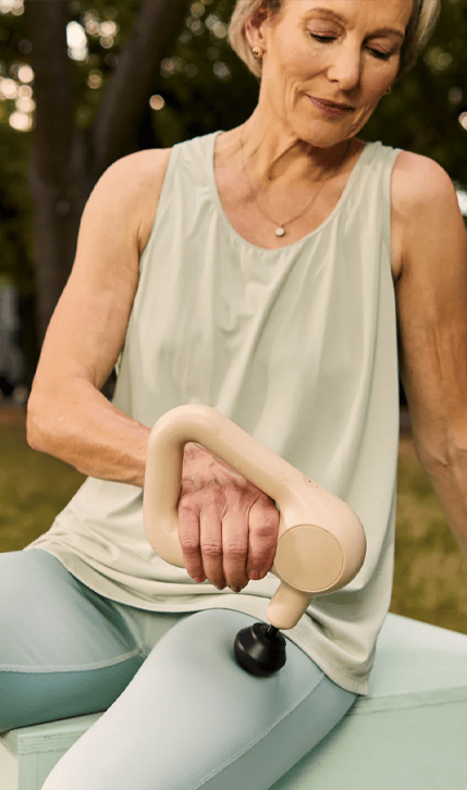 Woman using Theragun Relief on her legs outdoors.