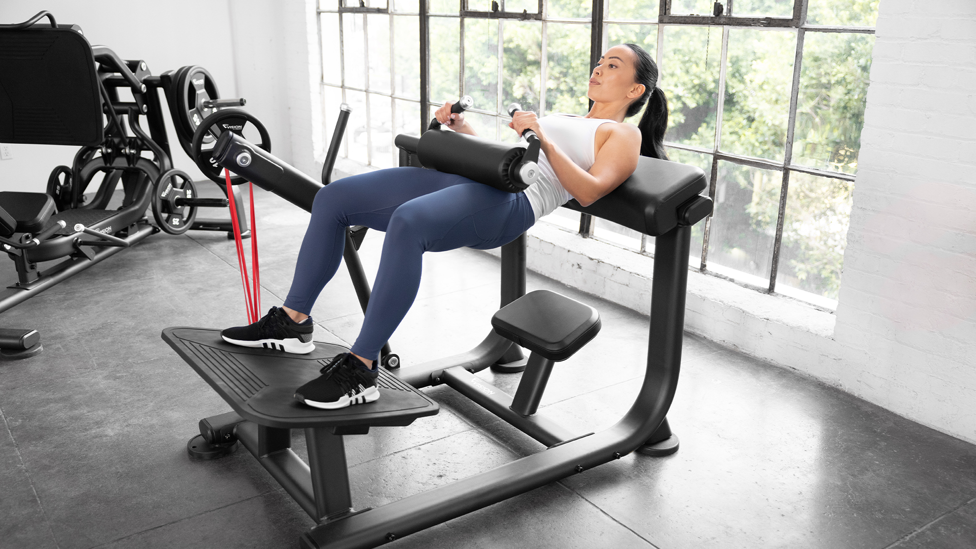 Woman using Vision Glute Trainer in small gym setting