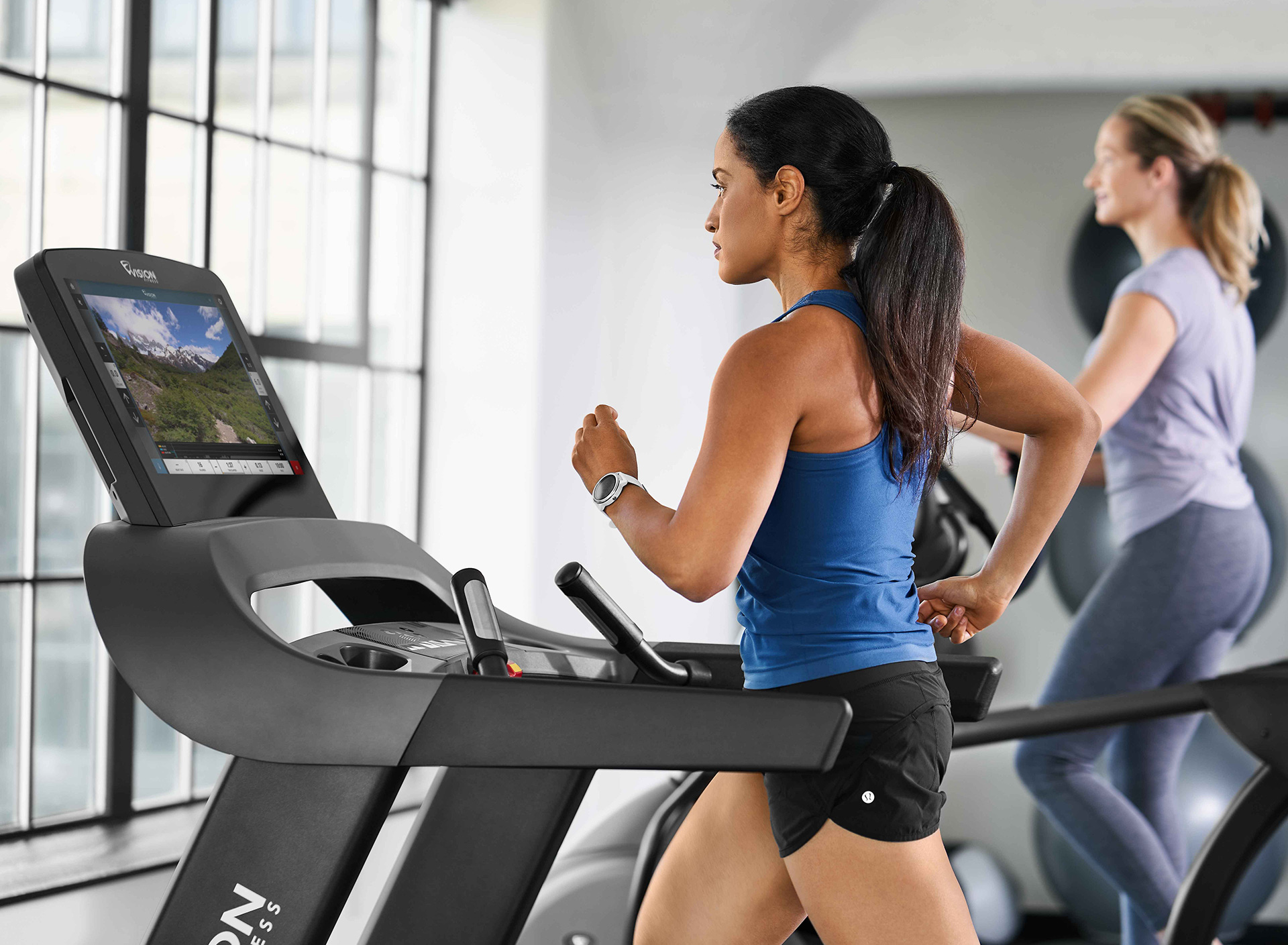 Woman running on treadmill and woman working out on elliptical in gym