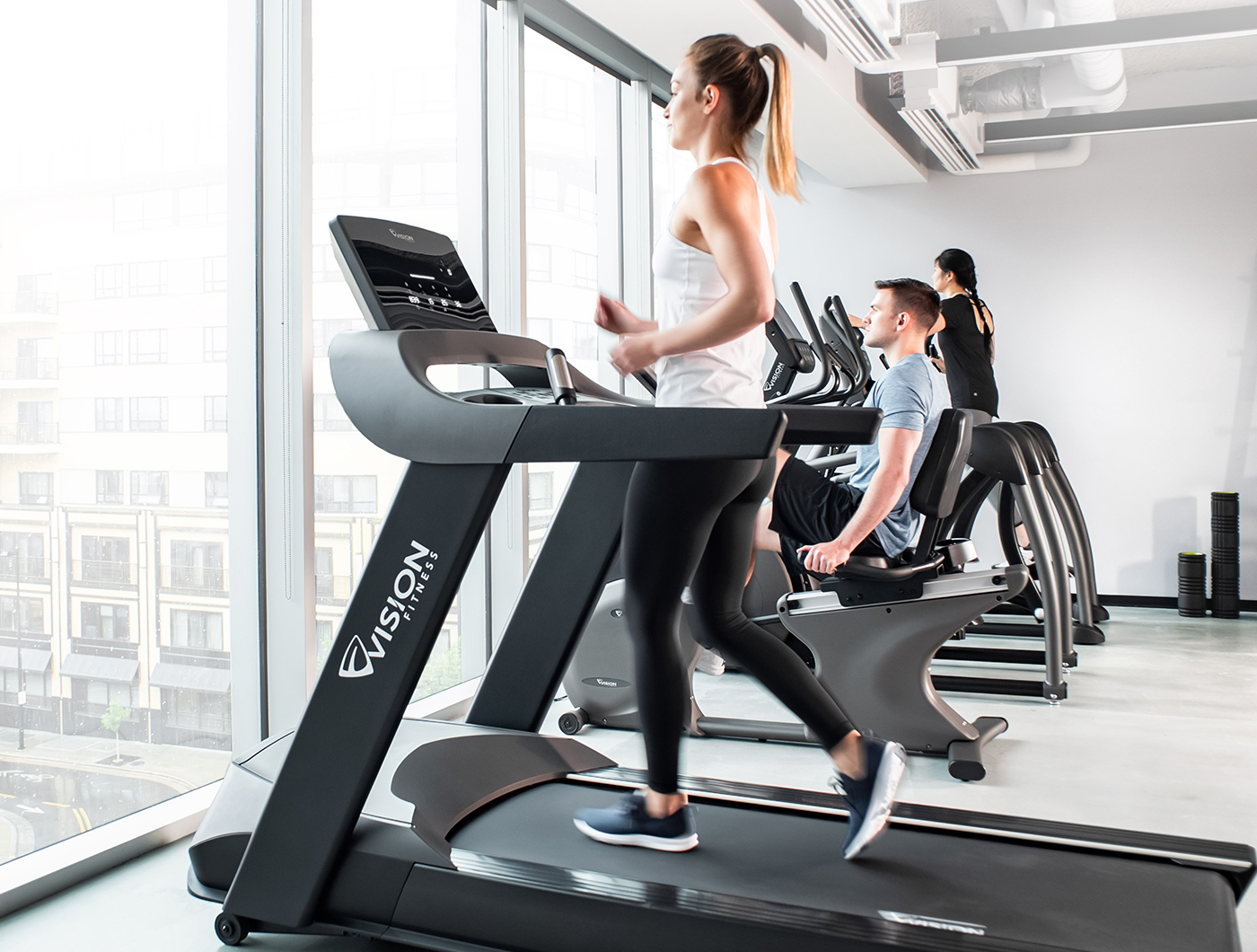 Woman walking on Vision treadmill, man riding Vision recumbent bike, and woman using Vision ellipitcal in apartment gym facility